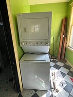 Full view of stacked washer and dryer against a green wall, showing overall condition and setup.