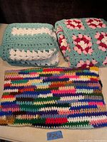 Three folded crochet blankets laid out on a flat surface showing different color patterns and textures.