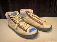 Pair of Penguin high-top leather upper shoes in cream and brown with white laces and black soles, displayed from side angle on neutral background