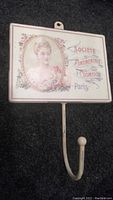 Full view of towel hook mounted on black surface showing porcelain sign with woman's portrait and French text.