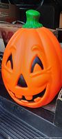 Photo of a 16-inch tall bright orange Halloween pumpkin blow mold with a green stem and a carved smiling face featuring triangular eyes, nose, and two front teeth.
