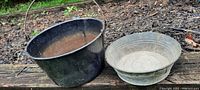 Large black pan and small galvanized tub side by side on wood surface outdoors