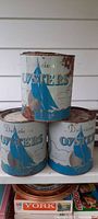 Full view of 3 stacked antique oyster cans showing blue sailboat graphics and lids with rust