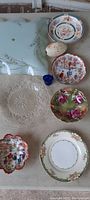 Top view of lot showing various antique decorative plates and glassware items arranged on a surface.