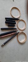 Photo showing three gold-tone Monet bracelets and several antique ink pens and lead pencils arranged on a flat surface.