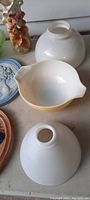 Close-up of yellow Pyrex bowl with two white glass lamp shades or covers and part of a vase base
