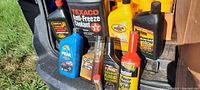 Photo of mixed automotive oils and fluids including Texaco antifreeze coolant, Peak fluid, No Leak oil treatment, Firestone power steering fluid and stop leak treatments, and other assorted containers.