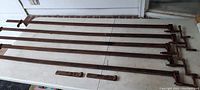 Five antique heavy steel shop clamps around 5 feet long each, laid out on a white surface, showing full length and mechanism ends.