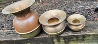 Three brass spittoons of descending size arranged on a wooden surface outdoors.