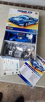 Open box showing blue metal body of Ferrari GTO Pioneer 1986 car model, plastic bags with parts, instruction manual, and decal sheets.