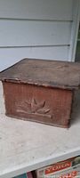 Old tramp art box showing worn fabric exterior and carved leaf design on side.