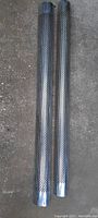 Two chrome perforated metal cylindrical pipe covers, each about five feet long, laid on ground showing full length and mounting brackets.