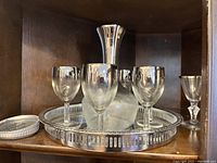 Bar set displayed on wooden shelf including silver-trim serving tray, decanter with silver detail, and four matching wine glasses with silver trim.