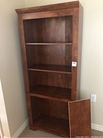 Full front view showing the wooden book shelf with three shelves and a bottom cabinet door detached and resting in front.