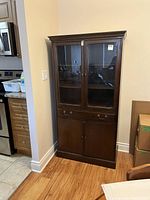 Full view of vintage style china cabinet against wall showing wood finish and glass panel doors.