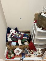 Wide view of Christmas lot including sweater, ornaments, figures, oven mitts and other holiday decor inside a cardboard box and on floor