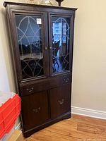 Front view of the dark wood corner china cabinet with decorative glass panel doors, two lower doors, and drawer.