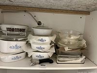 Photo of CorningWare white ceramic bakeware with blue cornflower pattern stacked with glass baking dishes and lids inside cabinet