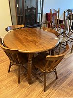 Round solid wood drop leaf kitchen table with four matching wooden chairs around it, placed on hardwood floor.