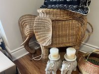 Overall shot of wicker elephant, two throw pillows on top, and two elephant candle holders with candles at base