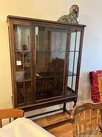 Front view of the vintage wooden china cabinet with glass paneled doors and decorative legs, showing overall structure and finish.