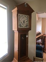 Full view of the grandfather clock showing its pine wood casing, chicken wire upper door with clock face, and lower closed storage door.