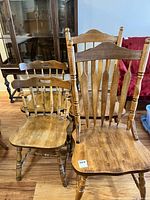 Front view of two wooden kitchen chairs, showing spindle backrests and contoured wooden seats, with visible scratches and wear.