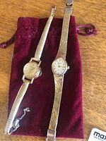Two ladies wristwatches displayed on a red velvet pouch including Movado and Accurist brands.