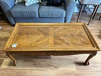 Top-down angled view of wood coffee table showing patterned wood grain tabletop, raised border, carved legs, and wear marks.