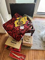 Photo shows a variety of sewing items including fabric, wooden and wicker boxes, sewing notion packs, and thimble on a chair beside a window