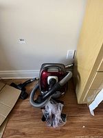 Shark canister vacuum cleaner with hose and attachments arranged on wooden floor next to wall and furniture