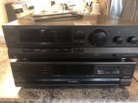 Front view of the Technics AV Control Stereo Receiver SA-GX130 stacked on top of the Technics Compact Disc Changer model SL-PD887 on a kitchen countertop, showcasing the control buttons and display screens.