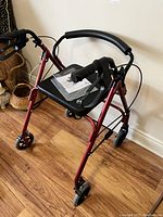 Red 4 wheel walker with brakes and seat from an angled side view.