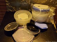 Image showing various used plastic Tupperware containers nested and stacked, some with blue lids and others clear, with one set still sealed in plastic.