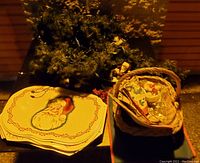 Photo showing green Christmas garland with lights, stacked Santa-themed placemats, woven basket with napkins and small items on black surface