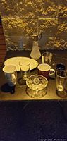Shows assortment of glassware on dark surface including textured glass pitcher, candy dishes, mugs and drinking glasses.