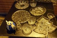 Table display of clear glass serving platters, candy dishes, bowls, a small glass pitcher, and a blue and white ceramic teapot.