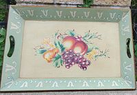 Rectangular wooden tray with green edges and white decorative motifs. Center has hand-painted fruit including grapes and pears. Carved handles on shorter sides.