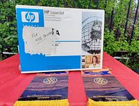 Photo of the original box of the HP LaserJet black ink cartridge labeled for 45II Printer with promotional Rotary Club items on red table.