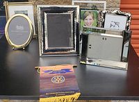 Multiple small picture frames of various styles and materials arranged on a black table surface with a Rotary Club banner in front.