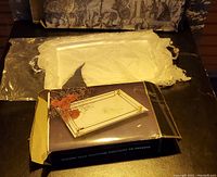 Photo shows a silver rectangular platter with decorative edge and handles, a mirrored vanity tray with a reflective surface and silver handles, along with the vanity tray's original box and a lace-like protective cloth bag.