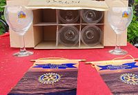 Two Leffe branded stemmed beer glasses shown outside cardboard packaging, with four glasses in partitions inside the box. Branding visible in gold with decorative color accent on each glass.