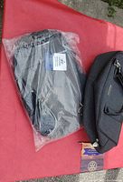 Two grey bags placed on a red surface, one soft foldable bag still sealed in plastic and one structured luggage bag with handles and shoulder strap.