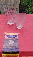 Two glass vases displayed on a red tablecloth outdoors with a Scarborough Twilight Rotary Club banner nearby.