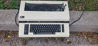 Front view of vintage typewriter showing beige plastic body, black keys, and power cord.