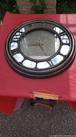 Photo of round wooden clock with mirror face and Roman numeral hour markers on red tablecloth.