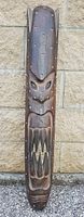 Front view of tall wooden carved decorative mask with detailed facial features and tooth design.