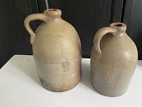 Front view of two vintage Quebec stoneware jugs, larger jug on left with handle and smaller jug on right.