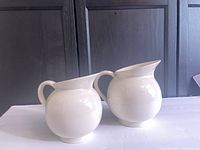 Front view of the two white ceramic jugs, showing their relative sizes and glossy finish.