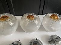 Three midcentury modern glass globes in opalescent white with amber yellow tops alongside their metal adapters, displayed on a surface.